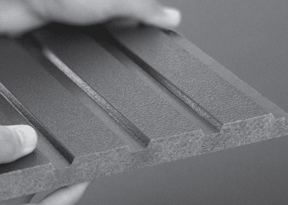 Close-up image of a hand holding a rectangular, textured material with evenly spaced, raised ridges running vertically along its surface. The material appears sturdy and industrial, possibly used in construction or manufacturing.