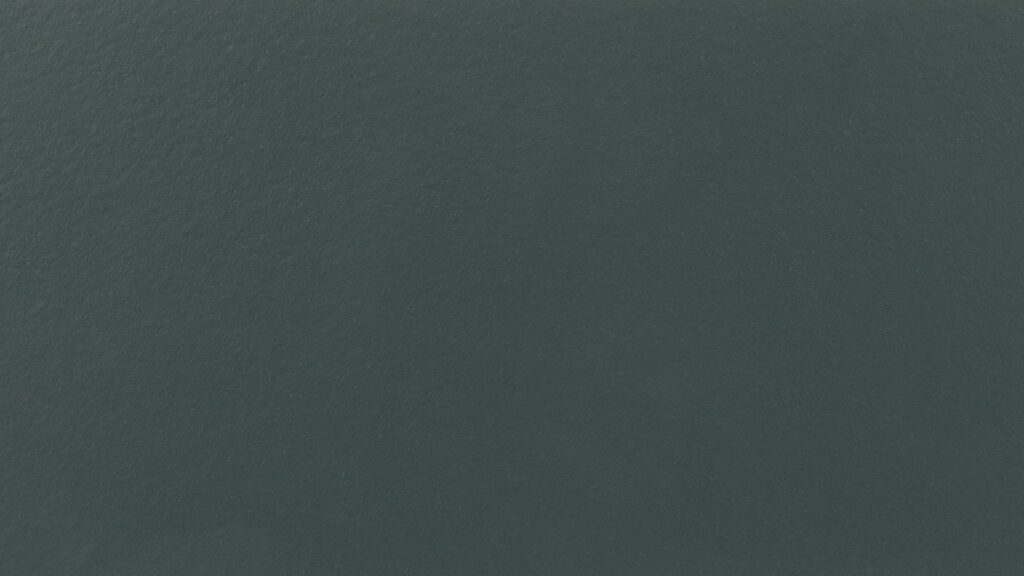 A close-up of a smooth, dark grey surface with a consistent texture. The lighting is even, highlighting the uniformity of the surface with slight variations in shading.