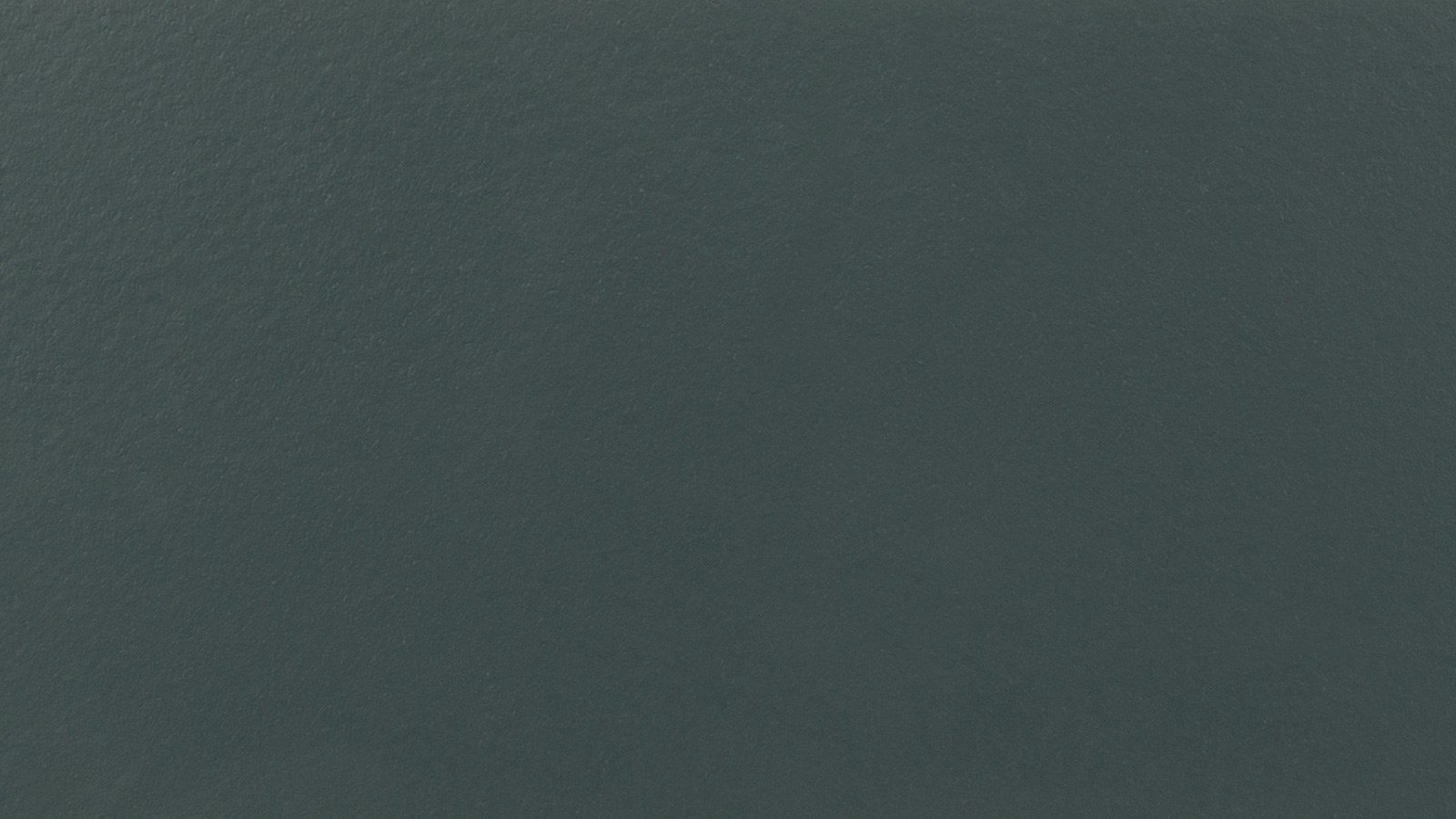 A close-up of a smooth, dark grey surface with a consistent texture. The lighting is even, highlighting the uniformity of the surface with slight variations in shading.