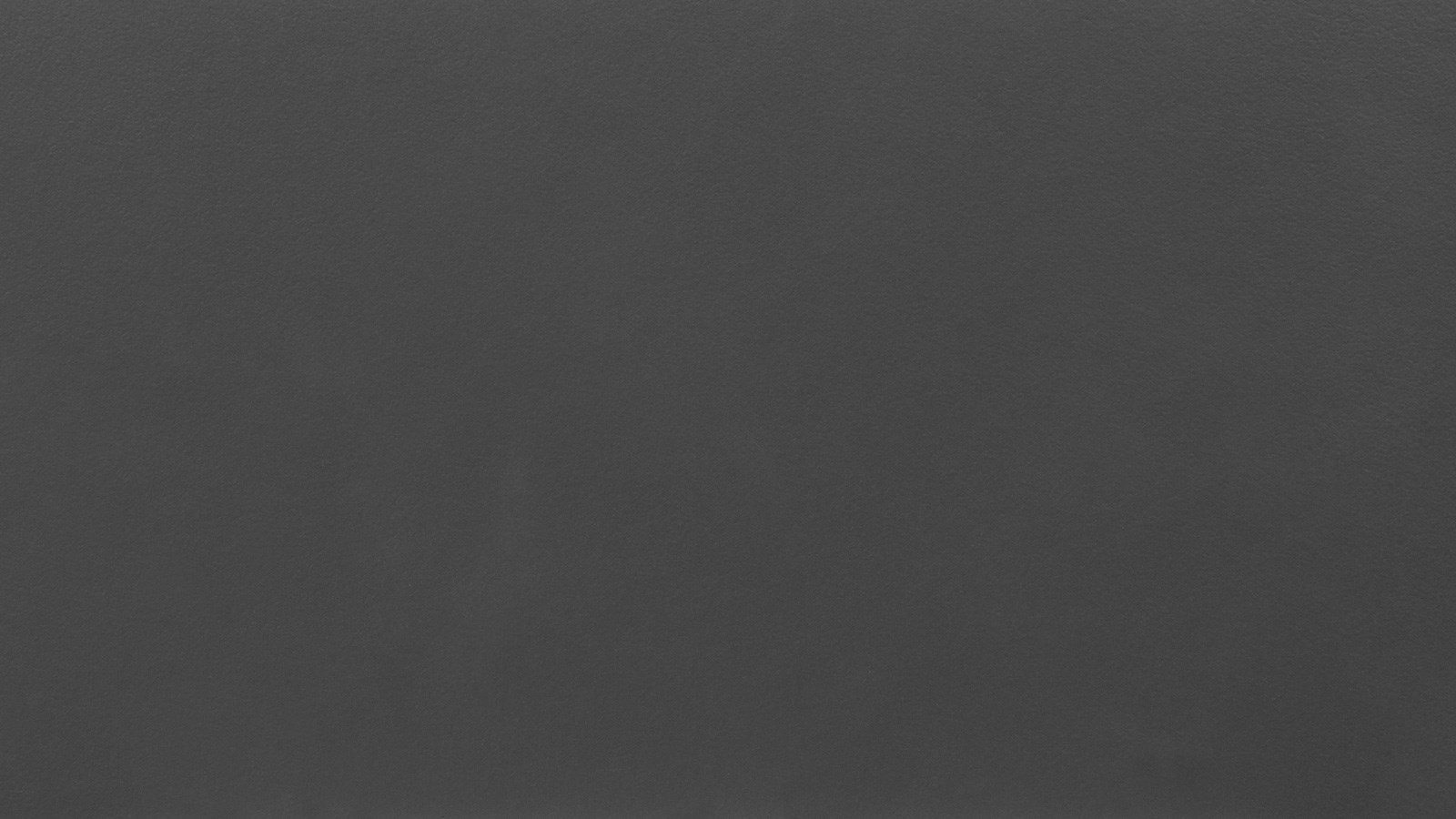 A close-up image of a dark grey, smooth leather texture with subtle variations in shading, showcasing its fine grain and matte finish. The surface appears uniform, without any distinct patterns or markings.