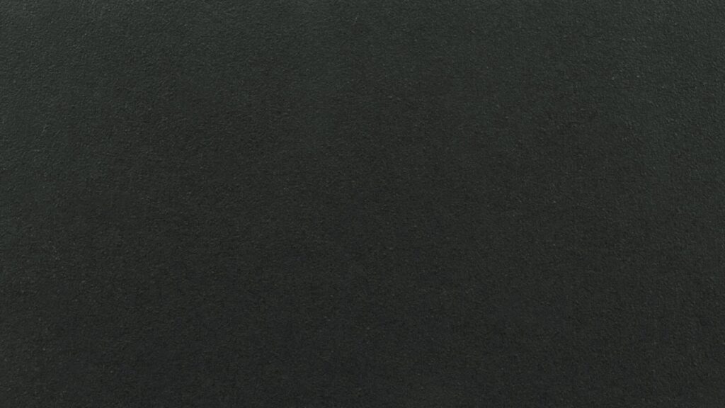 A close-up view of a dark textured surface, possibly black or very dark gray. The texture appears uniform and slightly rough, resembling materials such as asphalt, concrete, or a chalkboard.