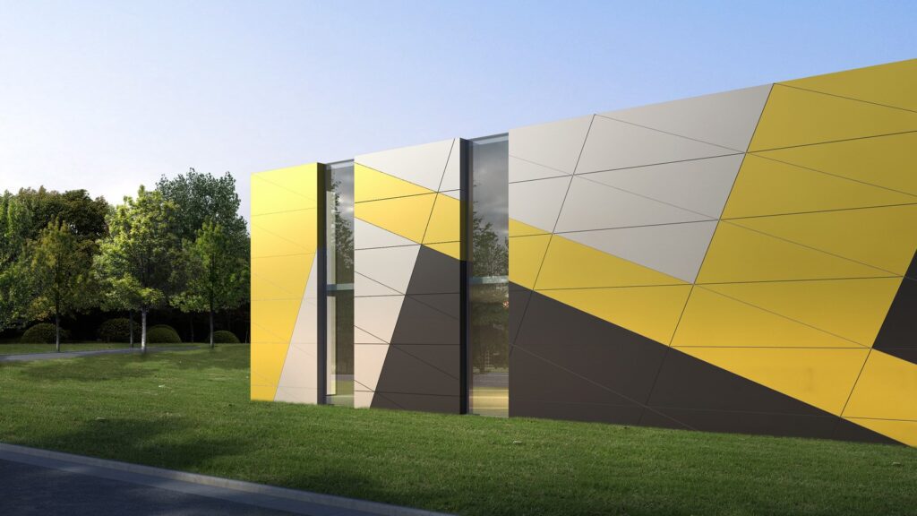 A modern building with a geometric facade featuring large yellow, grey, and black triangles. Tall trees are visible in the background, and a well-manicured lawn surrounds the structure. The sky is clear, indicating a sunny day.