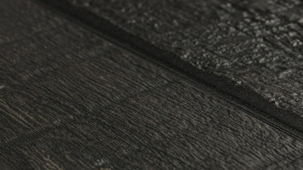 Close-up image of a dark, textured surface, possibly stone or wood. The appearance is rugged and uneven, with a combination of horizontal lines and grainy details, providing a sense of depth and a tactile, natural feel.