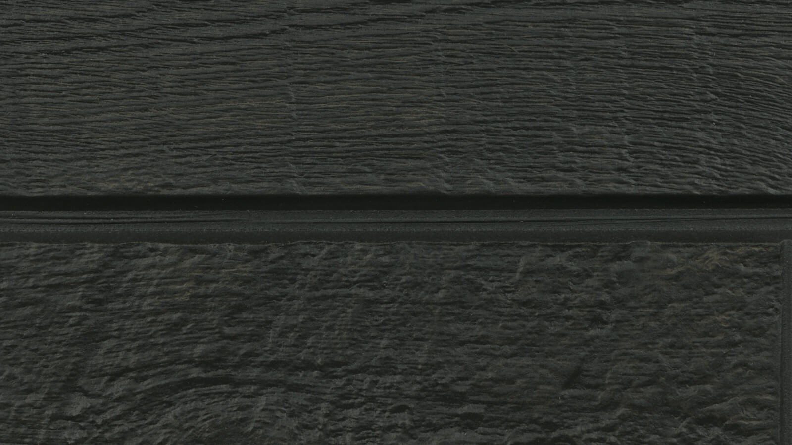 A close-up view of a dark, textured surface. The surface appears to be made of wood or a wood-like material with horizontal lines running through it, creating a rough, grainy pattern. The color is a deep charcoal or dark gray.