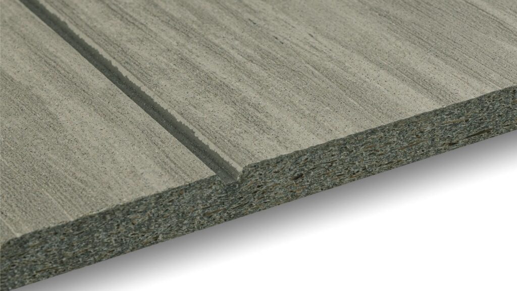 Close-up of a rectangular grey composite siding board with a grooved design. The texture appears rough and layered. The edge has visible layers showing the material composition. The background is plain and white.