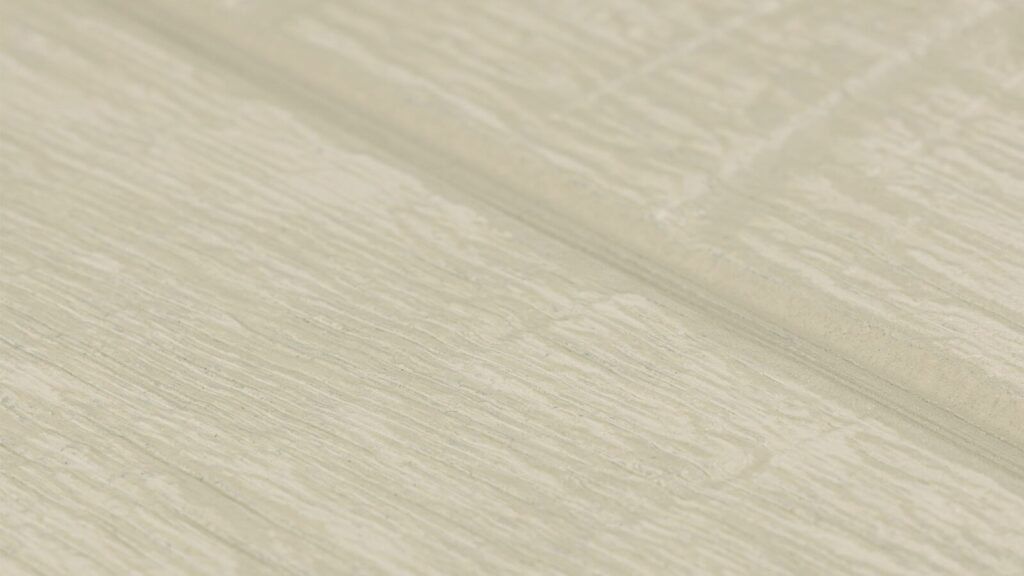 A close-up shot of a beige surface with a wood-like texture. The surface has a slightly raised grain pattern and a subtle groove running horizontally across the center.